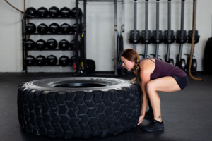 A woman is squatting on the tire in a gym.